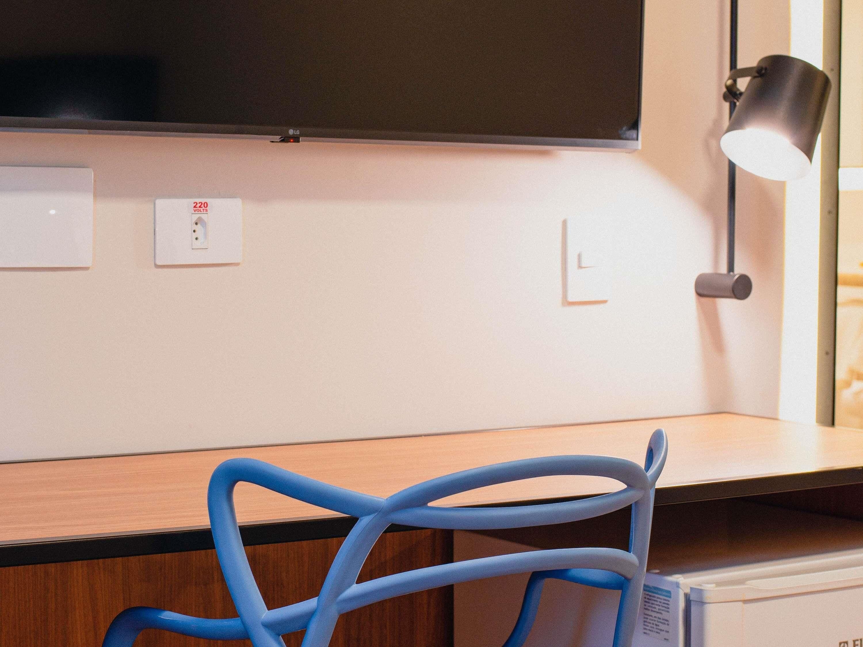 A modern room with a flat-screen TV mounted on the wall, a desk with a chair, and a lamp.