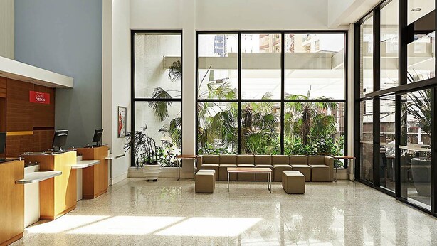A spacious lobby with a reception desk, seating area, and large windows offering views of greenery and buildings. - Ibis Curitiba Shopping (Curitiba)