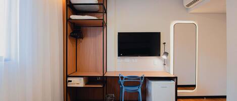 Habitación de hotel compacta con literas, un escritorio con silla, televisión, refrigerador pequeño y ventana con cortinas.
