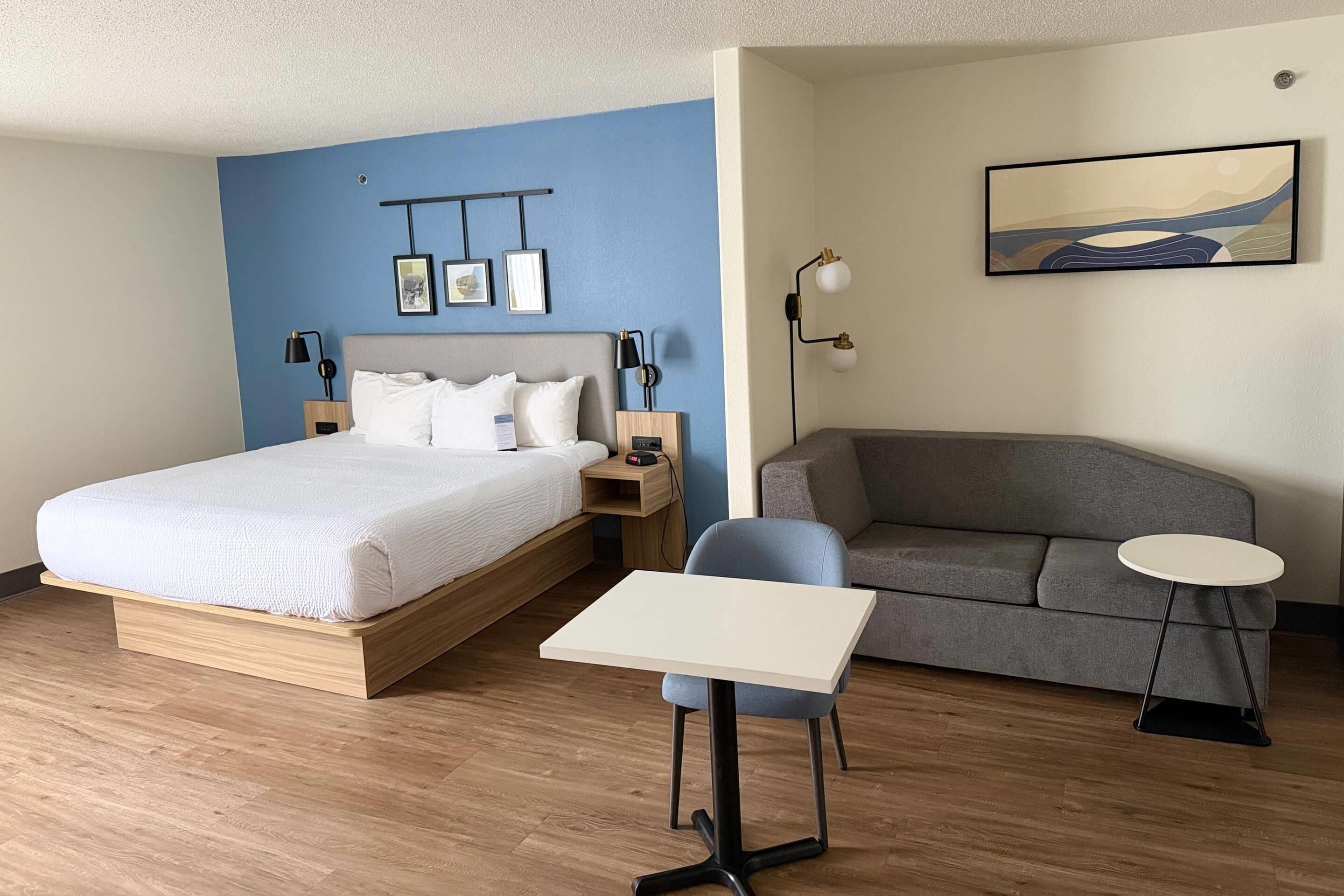 A hotel room with a bed, a sofa, a small table, and a wall-mounted artwork.