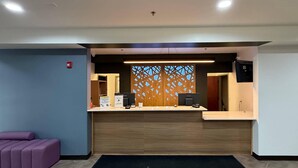 A reception desk with a wooden panel backdrop, a purple seating area, and a herringbone-patterned floor.