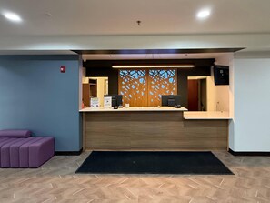 A reception desk with a wooden panel backdrop, a purple seating area, and a herringbone-patterned floor.