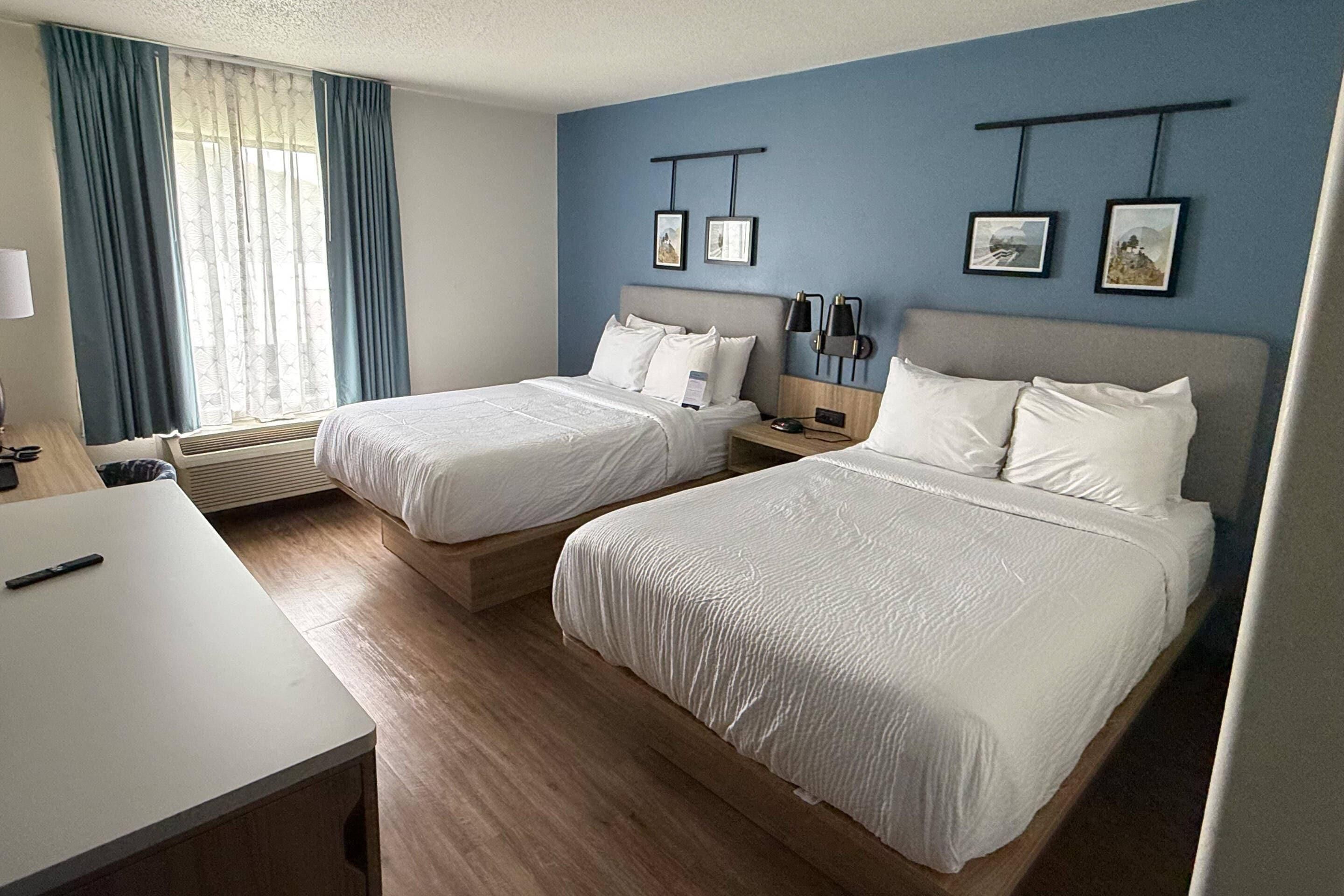 A hotel room with two beds, a desk, and a window with curtains.