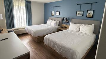 A hotel room with two beds, a desk, and a window with curtains.