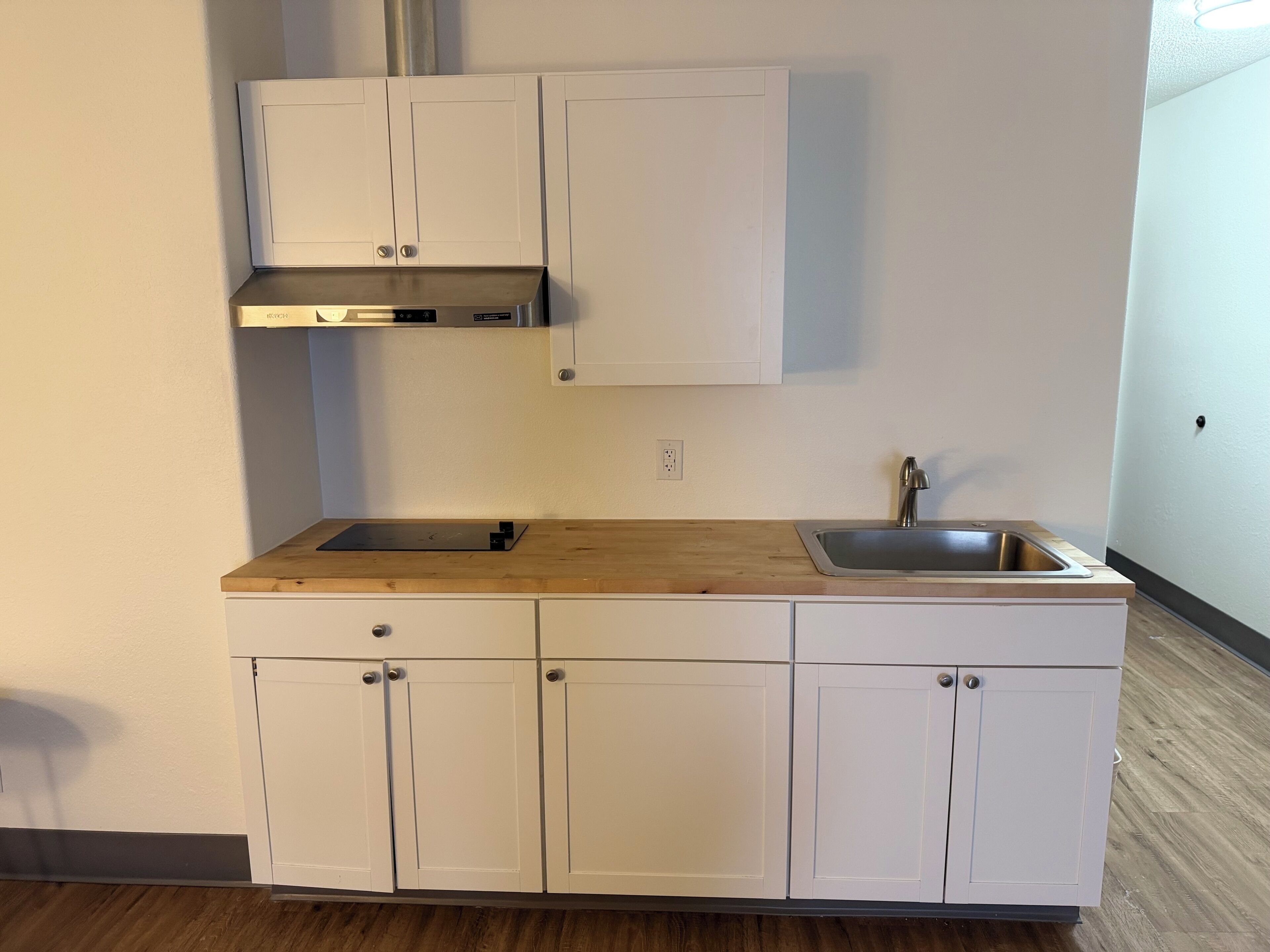 A kitchen with white cabinets, a wooden countertop, a stainless steel sink, and a built-in range hood.