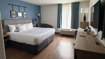 A hotel room with a bed, desk, chair, air conditioning unit, and a TV.