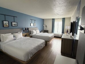 Quarto de hotel com duas camas, uma escrivaninha, televisão e janela com cortinas.