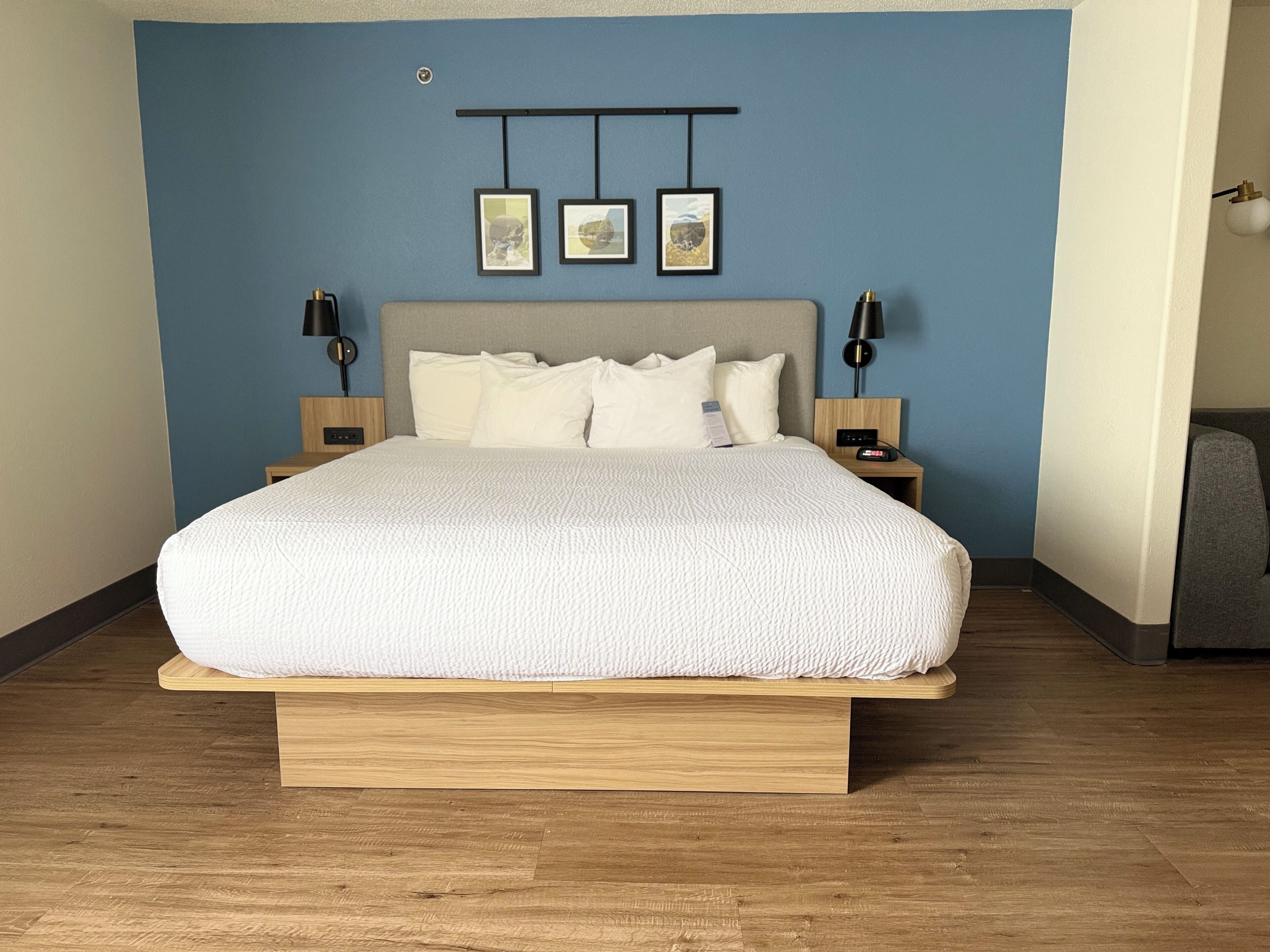 Un dormitorio con cama, cabecera, mesitas de noche, decoración en la pared y una mesita auxiliar.