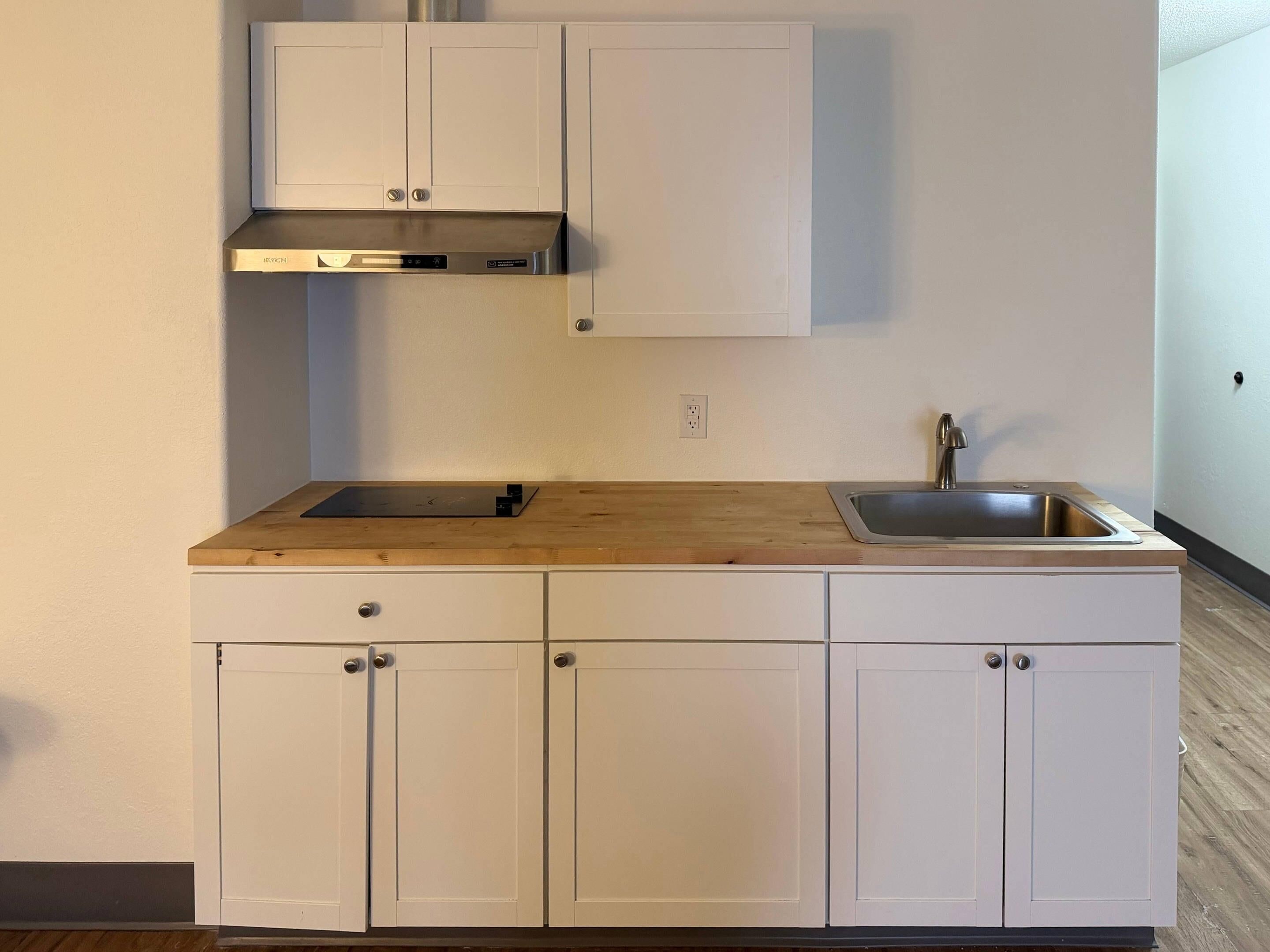 A kitchen with white cabinets, a wooden countertop, a stainless steel sink, and a range hood.
