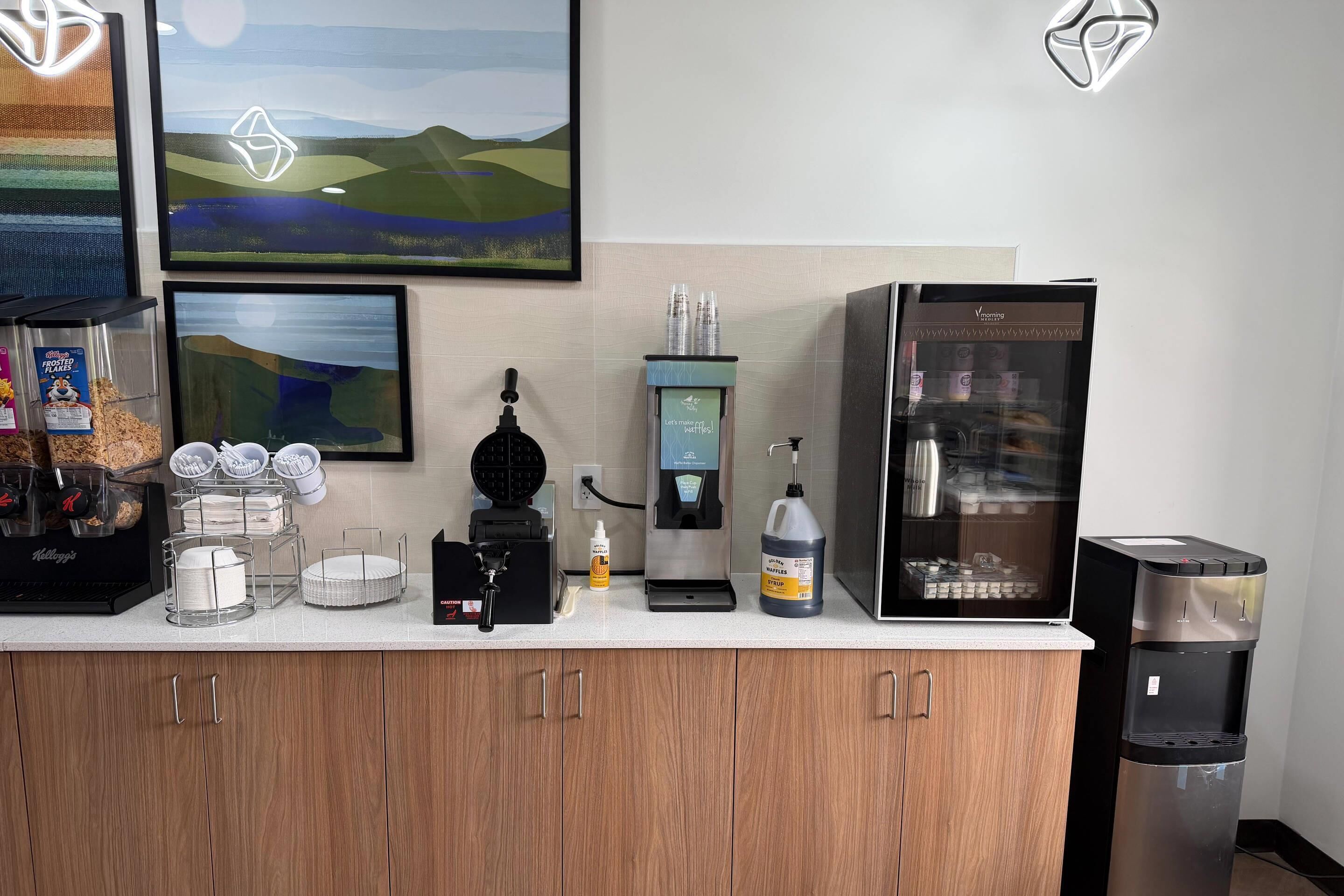 Une petite cuisine équipée d’une machine à café, d’un distributeur d’eau et de récipients de rangement.