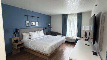 A hotel room with a large bed, bedside tables, a desk with a chair, a flat-screen TV, and a window with curtains.