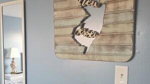 A wall with a decorative piece featuring a map outline and text, a mirror, and a light switch. - Pelican Point Motel (Point Pleasant Beach)