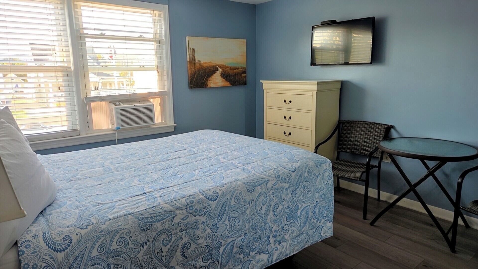 Une chambre à coucher avec un lit, une chaise, une commode, un tableau et un téléviseur.