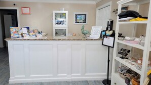 A reception area with a counter displaying various items, a framed picture, a sign prohibiting smoking, and shelves with decorative items. - Pelican Point Motel (Point Pleasant Beach)