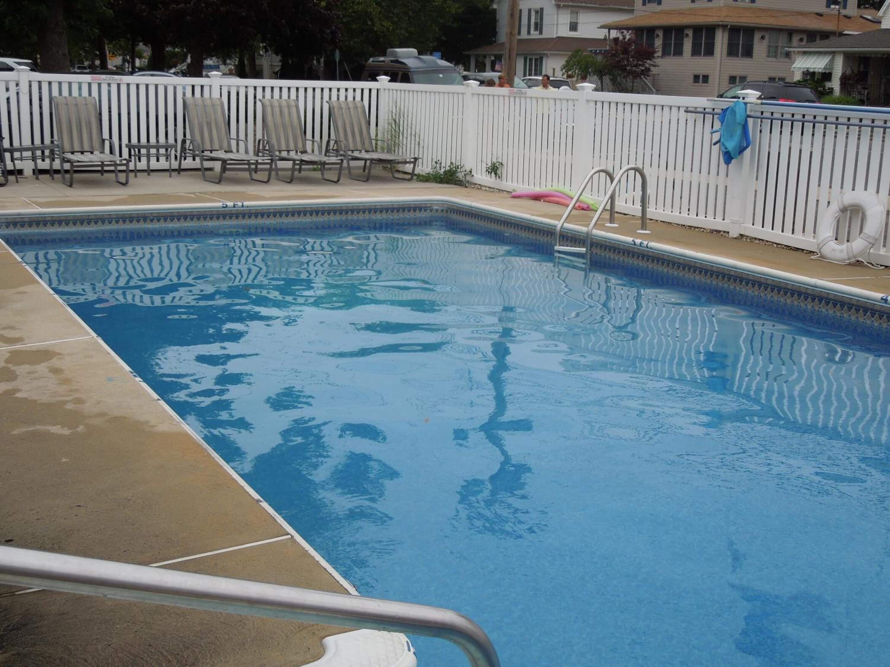 A rectangular swimming pool with a white fence and lounge chairs.