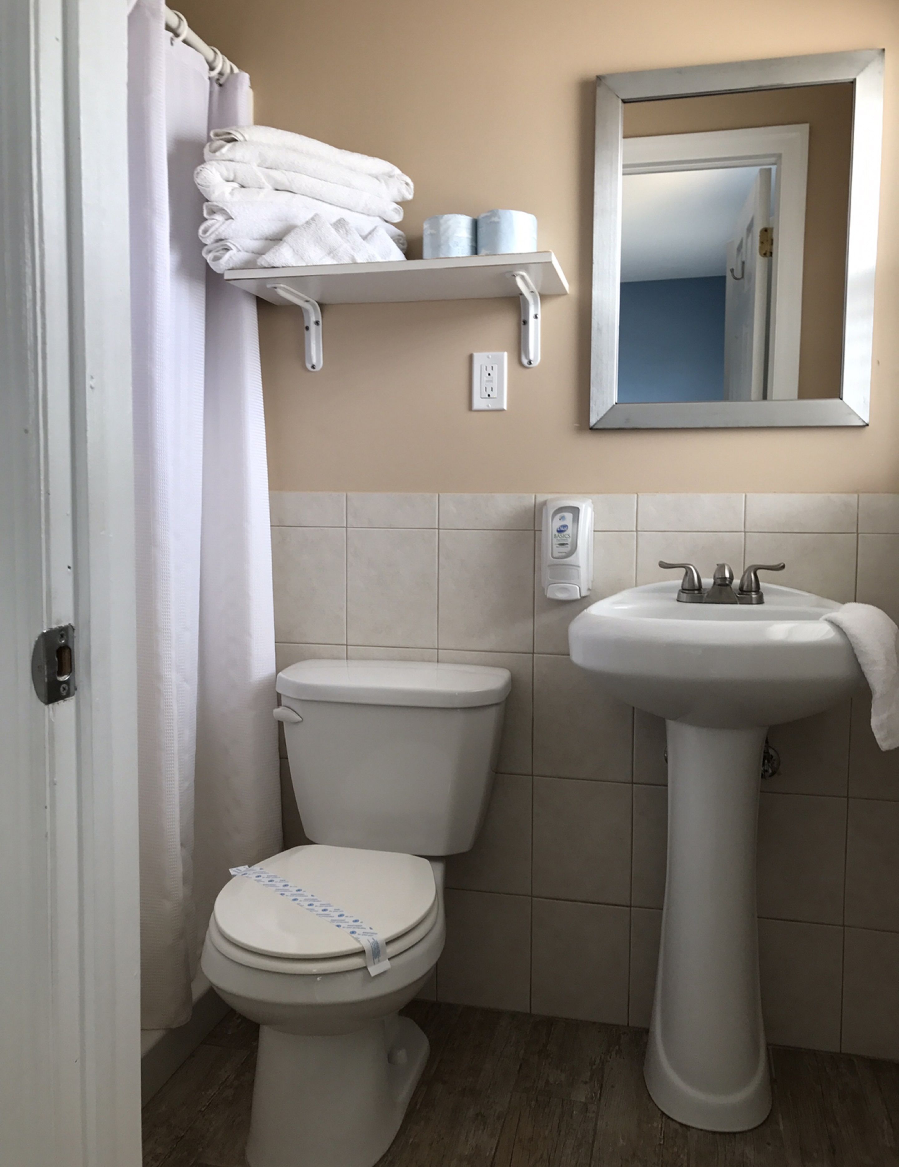 A bathroom with a toilet, a sink, a mirror, a towel rack, and a shower curtain.