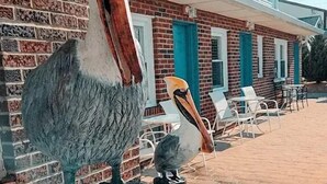 A large pelican sculpture on a post, a brick building with white trim, and outdoor seating. - Pelican Point Motel (Point Pleasant Beach)