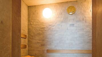 Eine Sauna mit Holzbänken und einer Ziegelwand, ausgestattet mit einer runden Leuchte und einem an der Wand befestigten Thermometer.