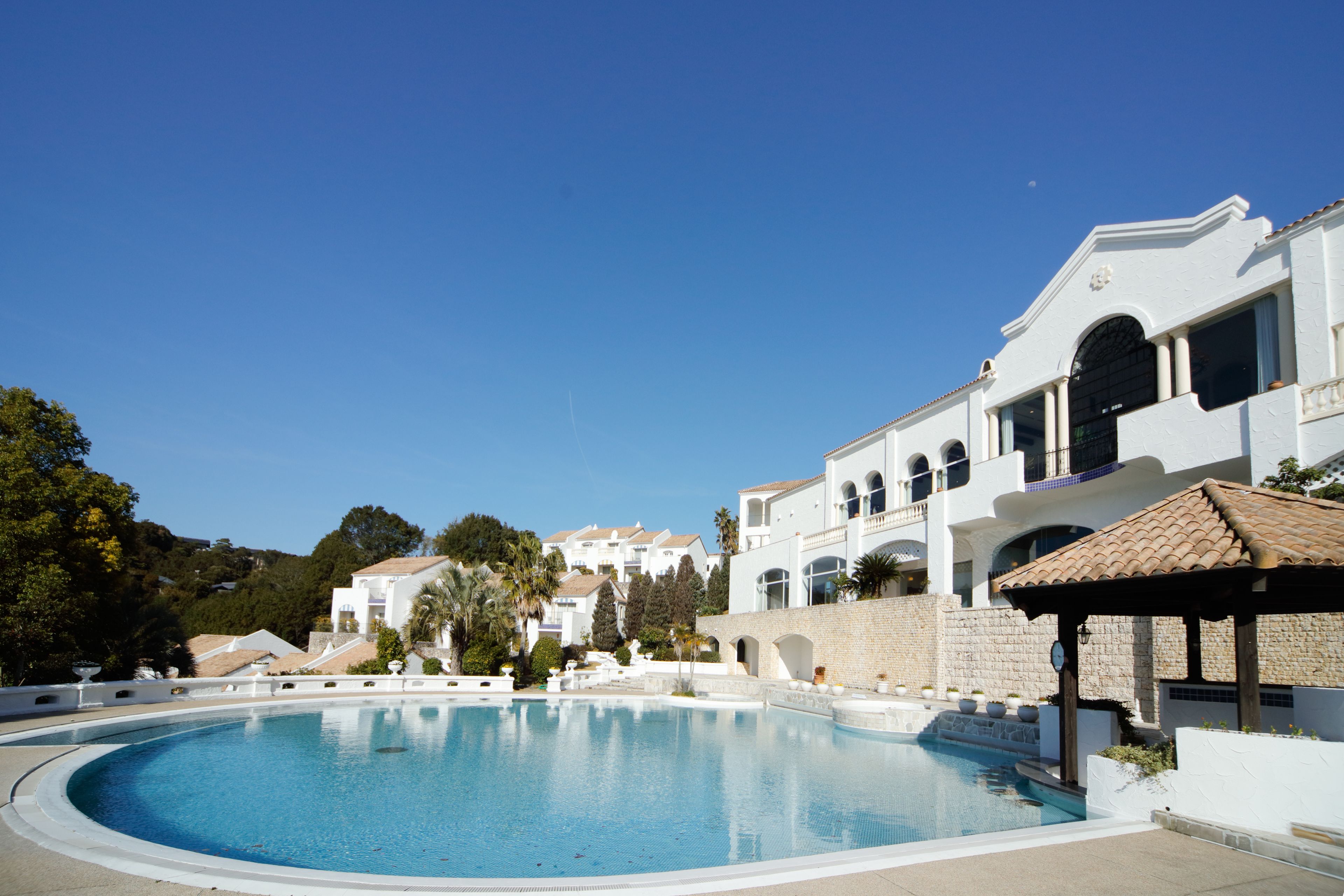 A swimming pool surrounded by a white building with multiple balconies and a stone wall.