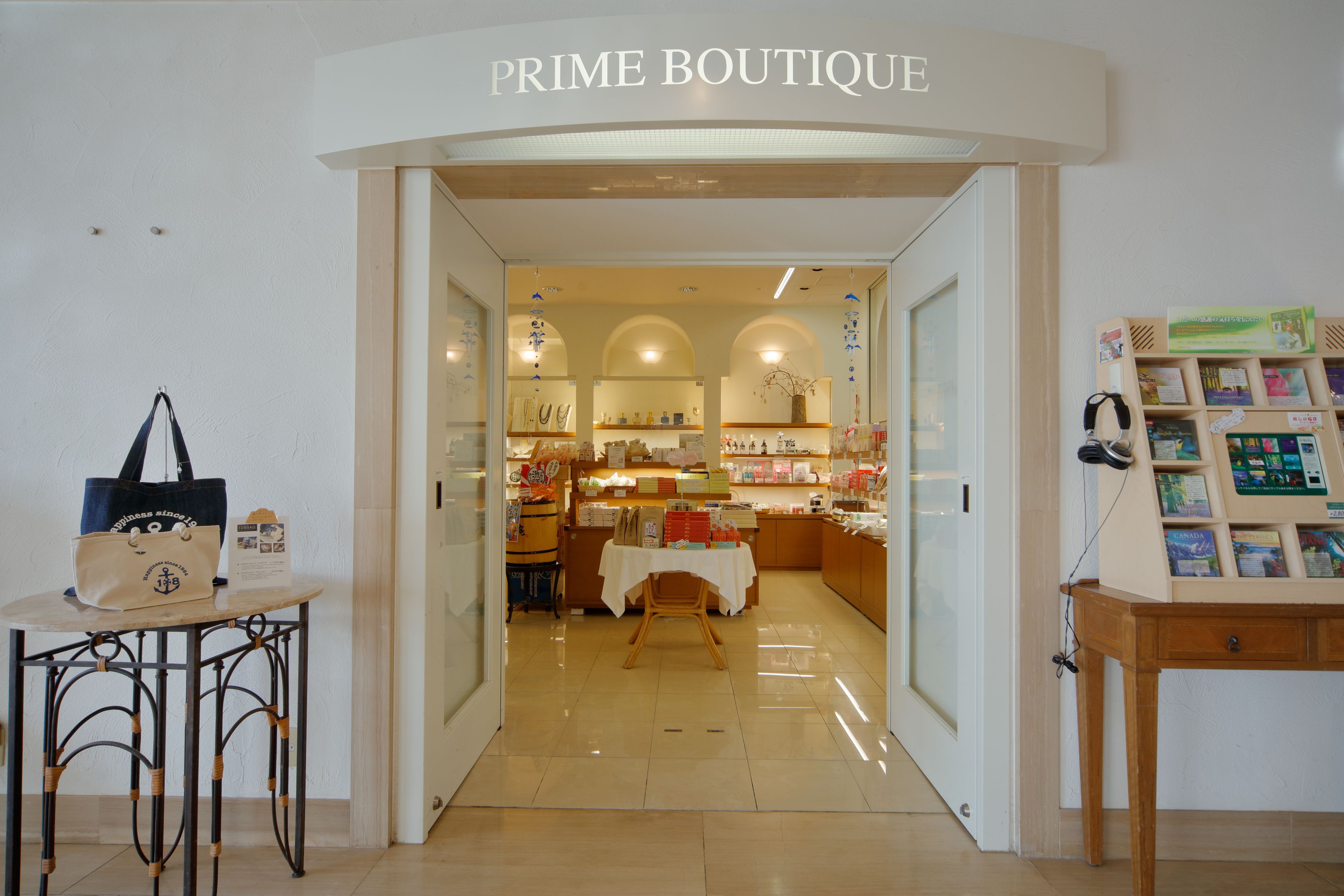L’entrée d’une boutique porte une enseigne indiquant « PRIME BOUTIQUE ». À l’intérieur, on trouve des étagères remplies de divers articles et une table de présentation recouverte d’une nappe blanche.
