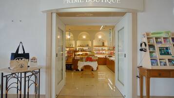 Der Eingang zu einem Boutique-Geschäft mit dem Schild "PRIME BOUTIQUE". Innen sind Regale mit verschiedenen Artikeln und ein Tisch mit weißer Tischdecke zu sehen.