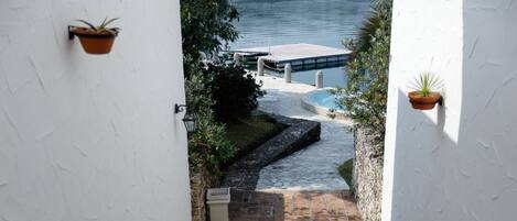 A pathway leading to a pool area with a stone-tiled floor and potted plants on the walls.