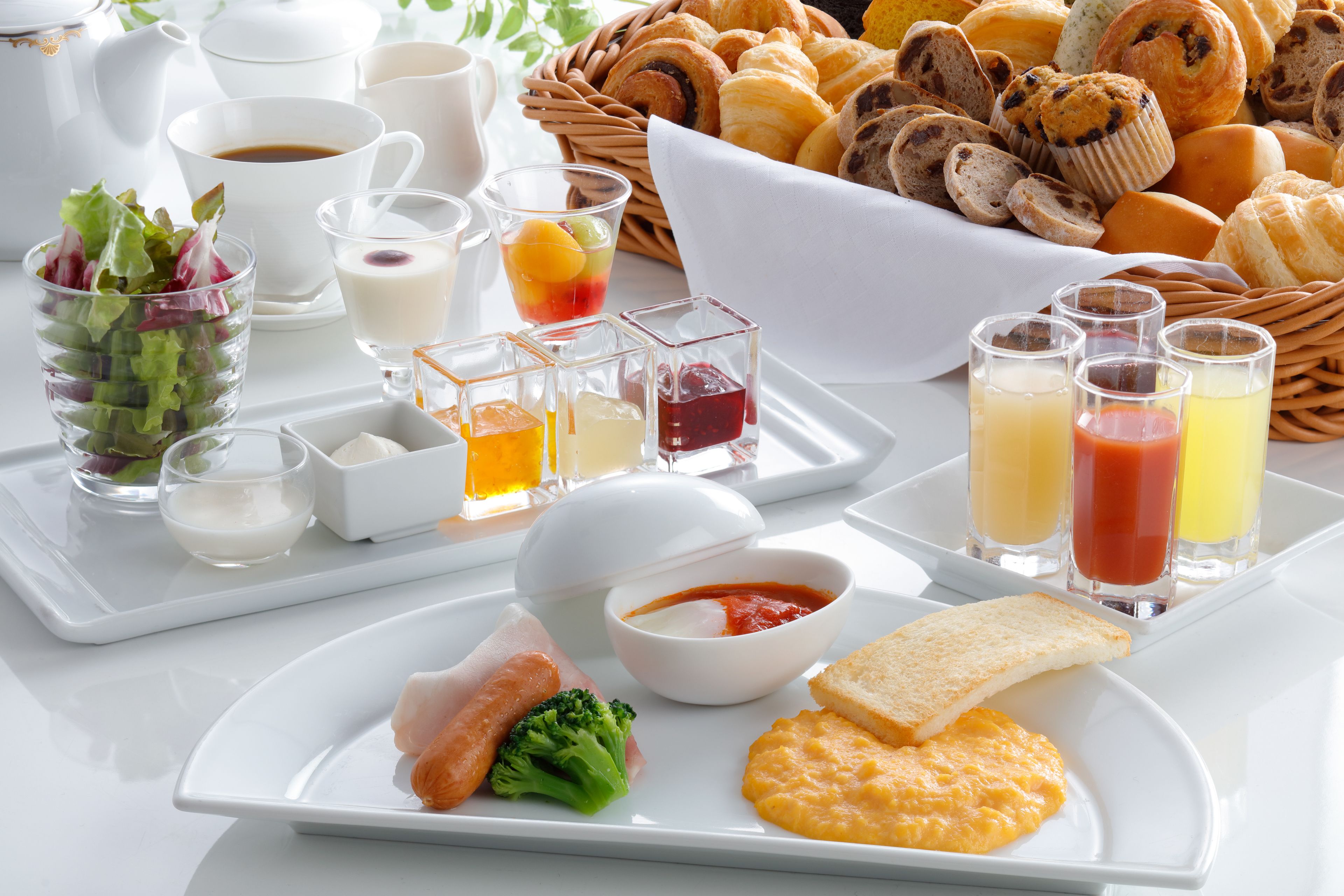 A breakfast tray with croissants, muffins, and pastries, along with a plate of eggs, toast, and a salad.