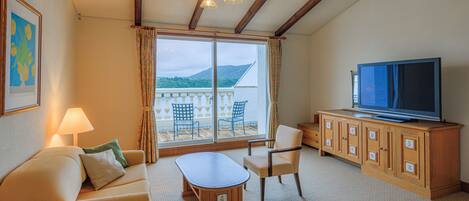 Ein Hotelzimmer mit Balkon, einer Couch, einem Fernseher und einem Holzschrank.