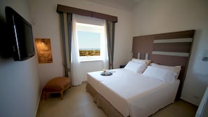 Una camera da letto con un letto, una panca, una TV, una finestra con tende e vista sul paesaggio.