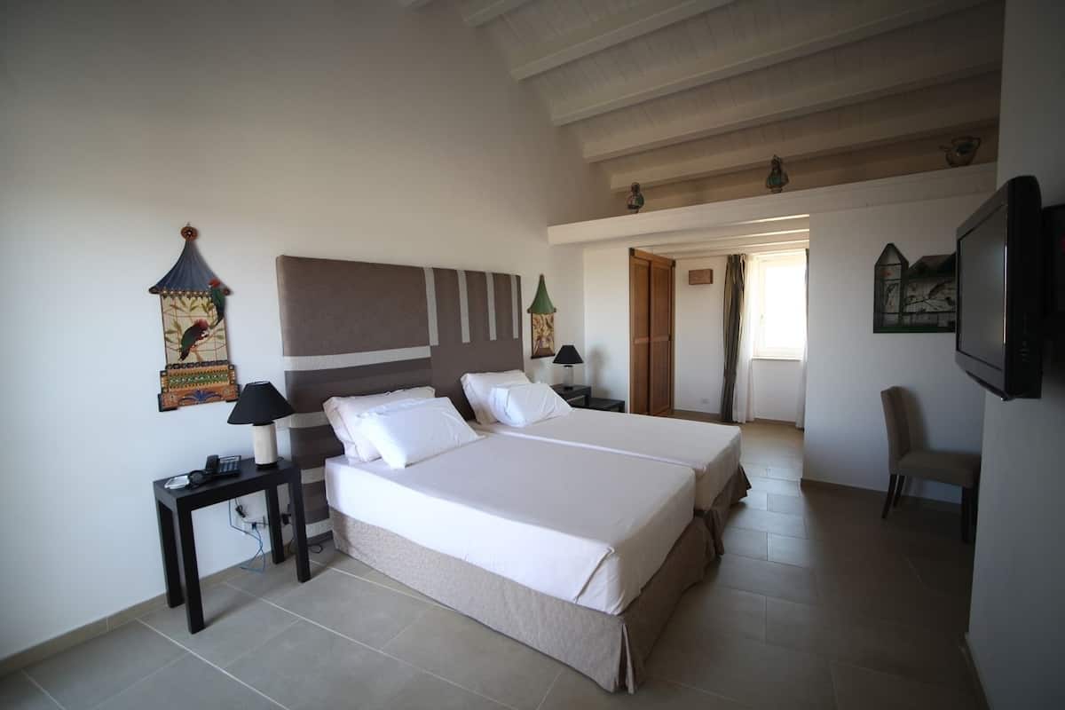 Ein Schlafzimmer mit einem großen Bett, einem Nachttisch, einer Lampe, einem an der Wand montierten Fernseher und einer Tür zu einem anderen Raum.