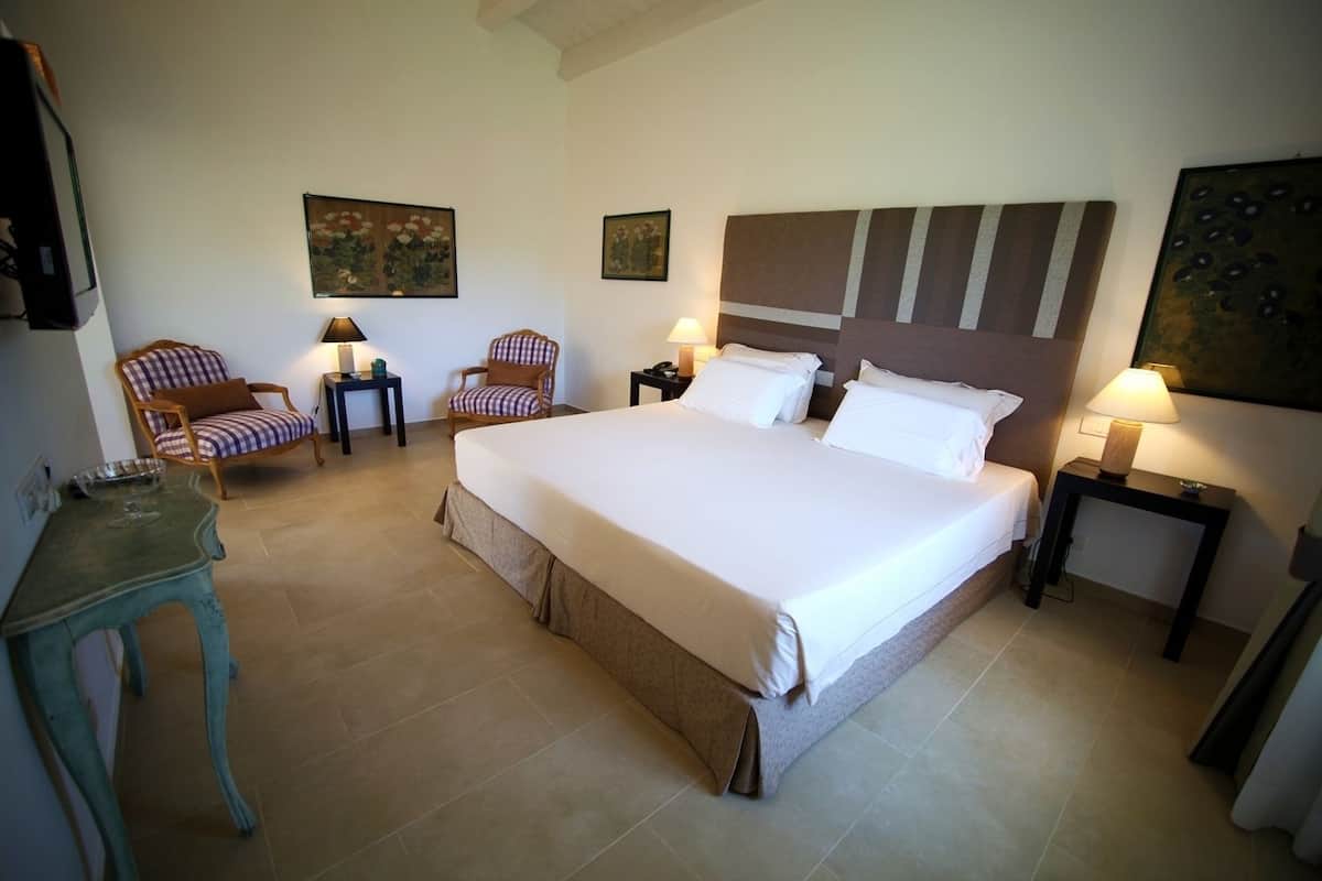 Ein Hotelzimmer mit einem großen Bett, zwei Sesseln, einem kleinen Tisch und Bildern an den Wänden.