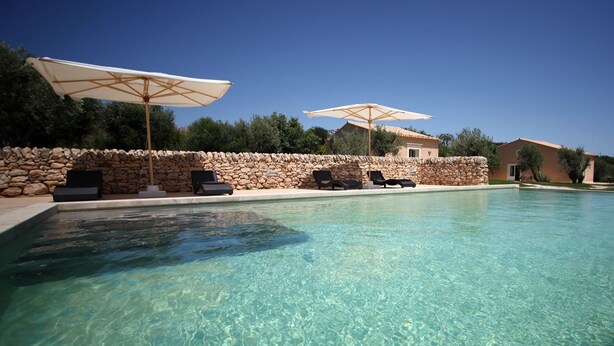 Una piscina limpida con lettini e ombrelloni, circondata da mura in pietra e un edificio in pietra.