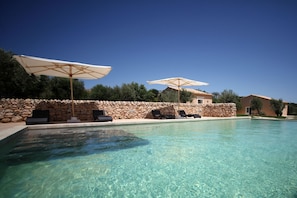 A clear swimming pool with lounge chairs and umbrellas, surrounded by stone walls and a stone building. - Antica Locanda del Golf (Ragusa)