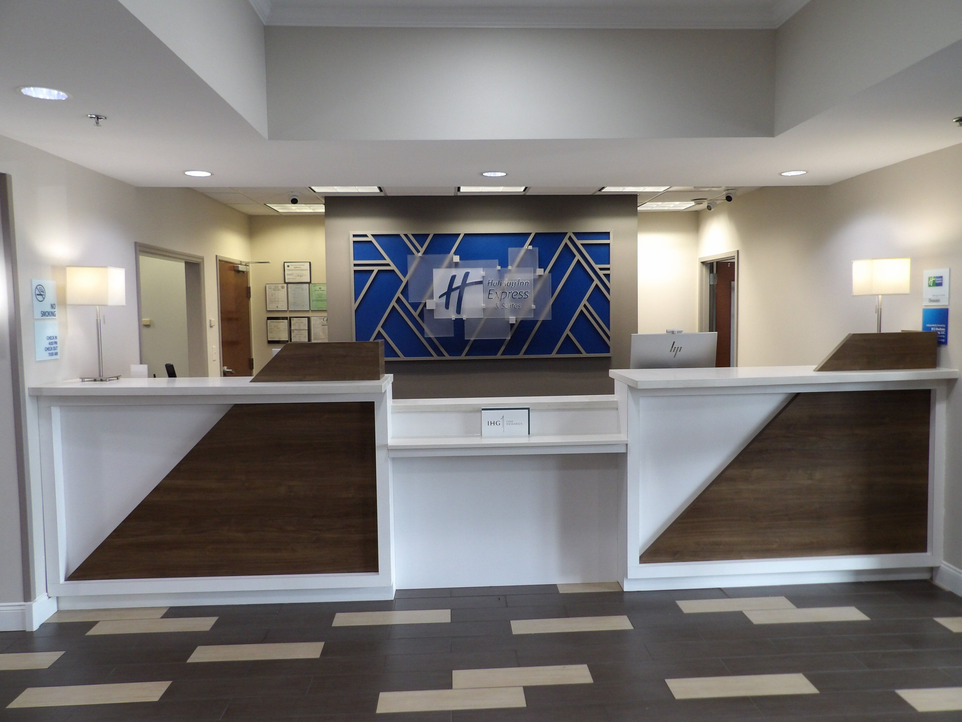 Un área de recepción con diseño moderno, que incluye un mostrador de recepción, una decoración mural geométrica azul y una distribución limpia y ordenada.