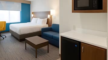 A hotel room with a bed, a desk, a chair, a microwave, and a refrigerator.