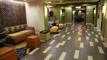 A hotel lobby with a sofa, armchairs, a small table, and a patterned rug.