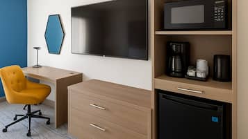A hotel room with a flat-screen TV, a microwave, a coffee maker, a refrigerator, a desk with a chair, and a blue accent wall.