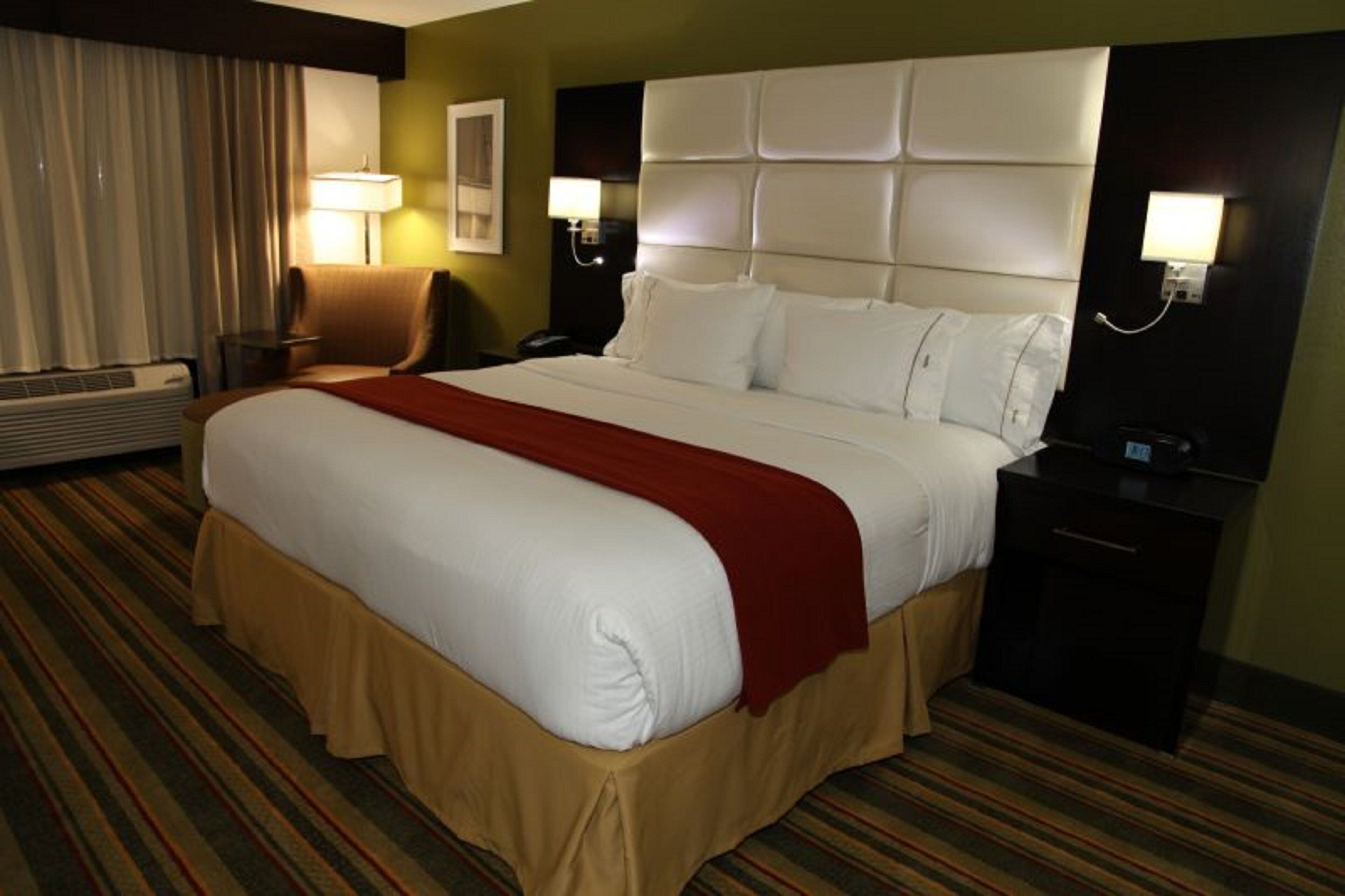 A hotel room with a large bed, a chair, a desk, a lamp, and a wall-mounted phone.