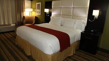 Ein Hotelzimmer mit einem großen Bett, einem Sessel, einem Schreibtisch, einer Lampe und einem an der Wand befestigten Telefon.