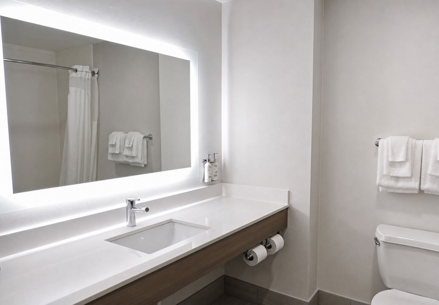 A modern bathroom with a large mirror, a white sink, and a toilet.