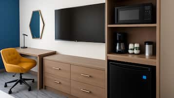 A modern hotel room with a desk, chair, flat-screen TV, microwave, coffee maker, and mini-fridge.