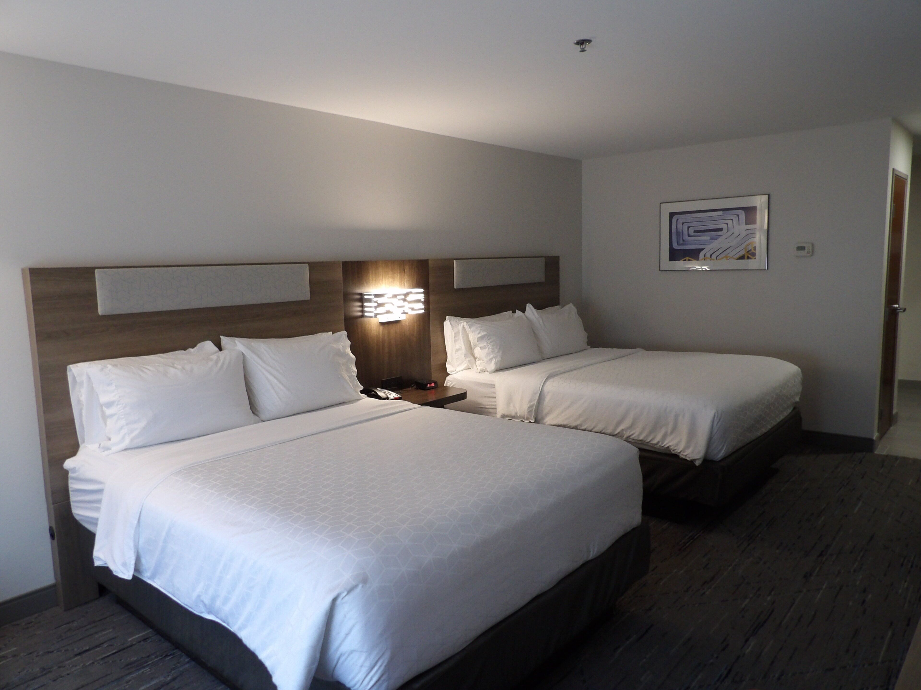 A hotel room with two beds, a nightstand, a wall-mounted light, and a framed picture.