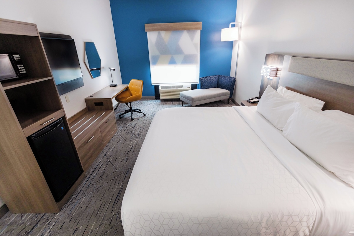A hotel room with a bed, a desk, a chair, a TV, and a window with blinds.