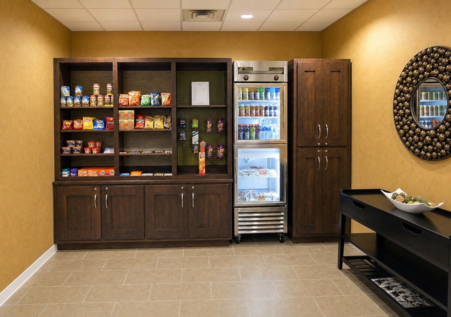 A kitchenette with a refrigerator stocked with beverages, a pantry with snacks, and a wooden cabinet.