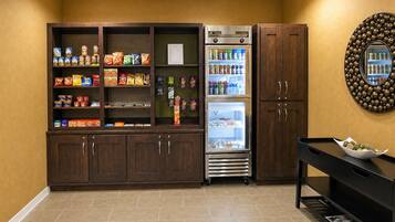 A kitchenette with a refrigerator stocked with beverages, a pantry with snacks, and a wooden cabinet.