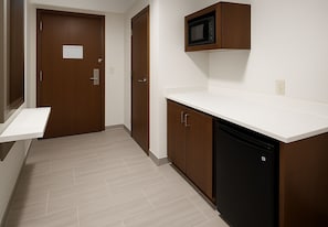 A hallway with a microwave above a white countertop, a dishwasher, and a door with a sign. - Holiday Inn Express & Suites Huntsville Airport by IHG (Madison)