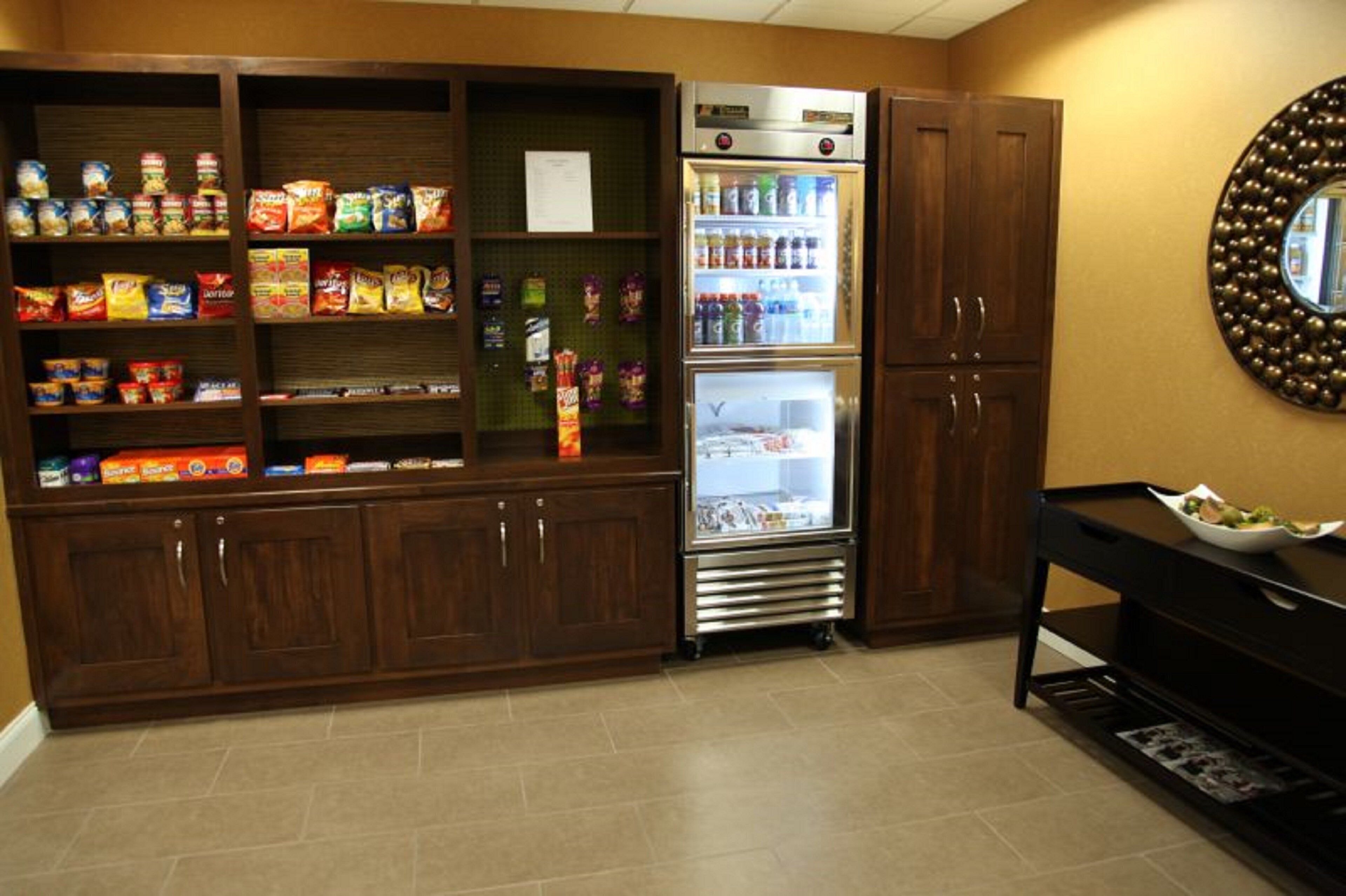 A kitchenette area with a refrigerator stocked with beverages, a microwave, and various food items on shelves.