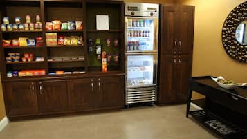 Una kitchenette con un refrigerador lleno de bebidas, un microondas y varios alimentos en estantes.