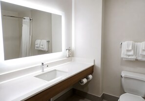 Een moderne badkamer met een grote spiegel, een witte wastafel, een houten badkamermeubel en een toilet.