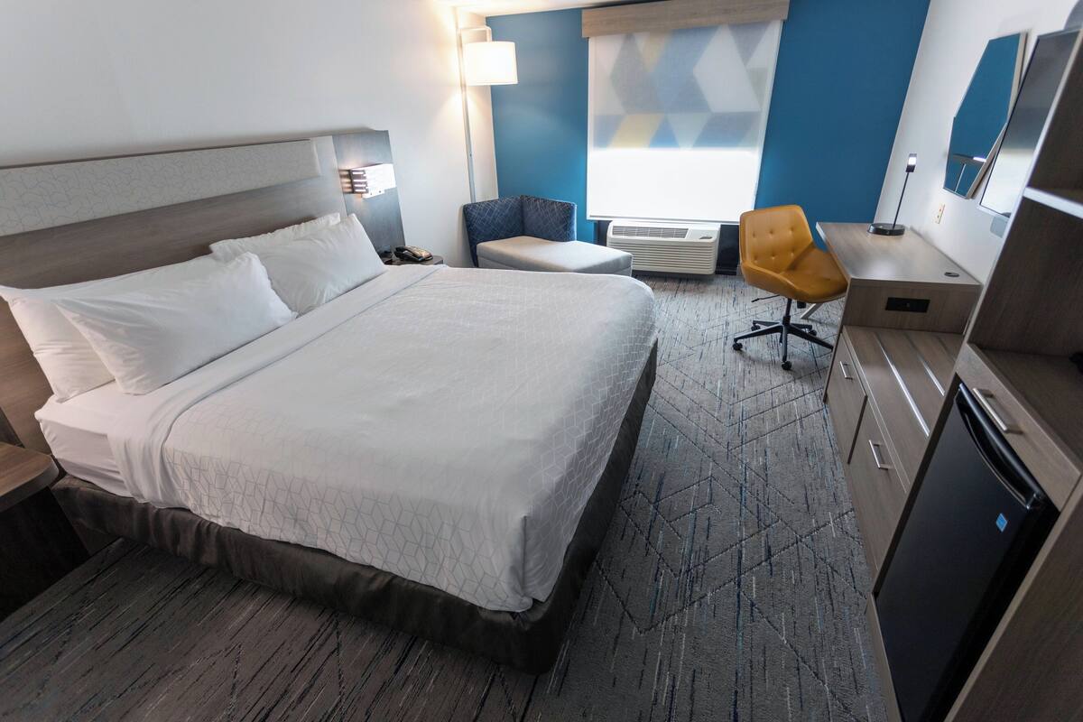 Habitación de hotel con una cama grande, un escritorio, una silla, una lámpara de escritorio, un aire acondicionado y una televisión.